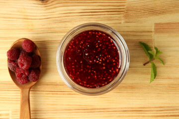 Glass bowl of raspberry jam with ingredients on wooden background