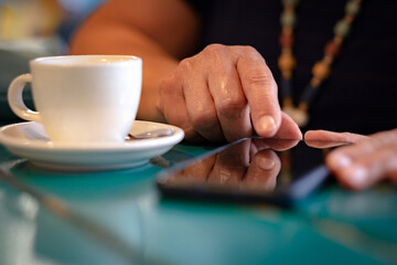 Close up on woman with white coffee cup on table, messaging with mobile phone. Sitting and enjoying tech and social