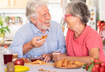 Cheerful caucasian couple having breakfast at home. Senior people relaxed and happy, enjoying food and drink