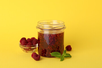 Jar of raspberry jam with ingredients on yellow background