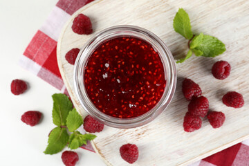 Jar of raspberry jam with ingredients on white wooden stand