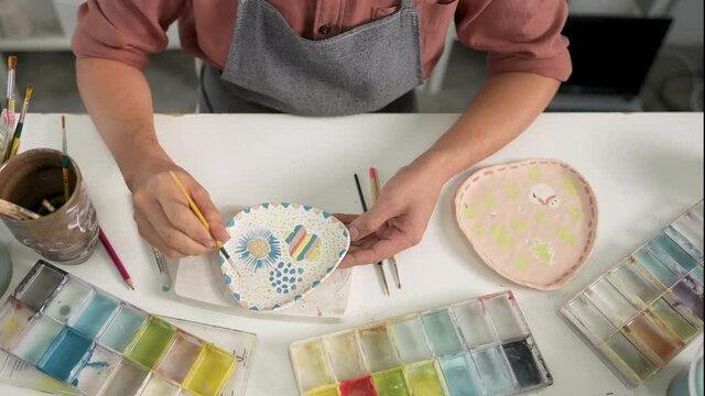 Asian LGBTQ guy learning color painting her self-made pottery at home. Confidence male enjoy hobbies and indoors leisure activity handicraft ceramic sculpture and painting workshop at pottery studio