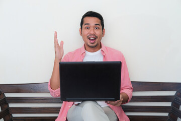 Adult Asian man showing excited face expression when working using laptop in his home