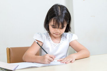 Fototapeta na wymiar Cheerful Asian little girl children student writing on notebook doing homework and self study at home. Education Homeschool Concept Stock Photo