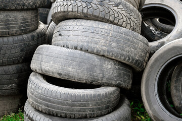 Pile of old dirty worn-out rubber tire tires on the grass. Concept of illegal landfills of rubber tires. Recycling concept. Garbage from old used rubber wheel tires on meadow. Environment pollution.