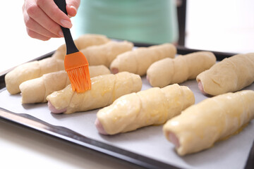 Female chef applies brush of egg yolk to croissants closeup