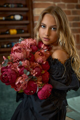 Teen girl in a black stylish dress with peonies in her hands in the interior of the restaurant