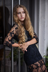 Teen girl in a black stylish dress against the background of glass doors