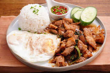 Crispy pork basil rice with fried egg, spicy food, in a round plate on the wooden floor.