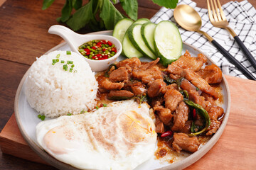 Crispy pork basil rice with fried egg, spicy food, in a round plate on the wooden floor.