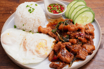 Crispy pork basil rice with fried egg, spicy food, in a round plate on the wooden floor.