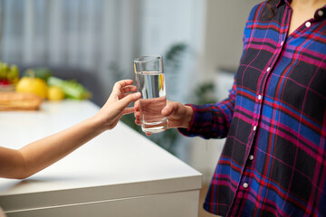 Cropped image of a little girl holding a glass of water in the kitchen with the young mother.