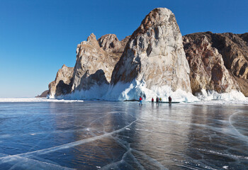 Frozen Baikal Lake. Group of young tourists ice skating on ice around Olkhon Island and admiring the beautiful Three Brothers cliffs. Magnificent winter landscape. Ice travel and outdoor activities