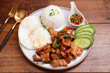 Crispy pork basil rice with fried egg, spicy food, in a round plate on the wooden floor.