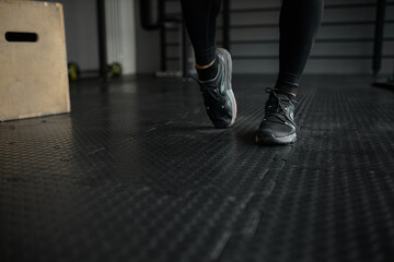 Crop shot of man feet in black sport shoes or sneakers moving on gym floor during intensive workout against sports equipment. People and active lifestyle. Aerobics, fitness, indoor sports