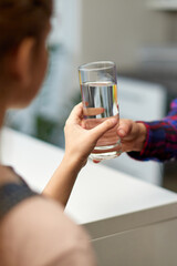 Cropped image of a hand little girl holding a glass of water in the kitchen with the mother.