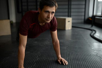 Sportive Caucasian man doing plank core exercise with straight hands at gym, training back press muscles looking ahead with concentrated face expression. Active lifestyle concept. Crossfit, fitness