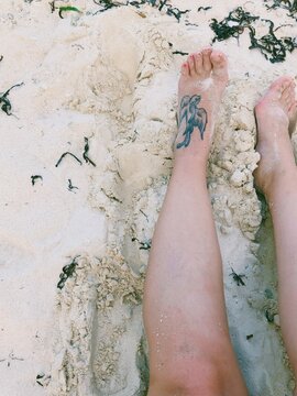 Overhead view of a woman's legs with a swallow tattoo on a sandy beach, Philippines