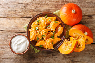 Delicious healthy orange pumpkin dumplings served with sour cream close-up in a plate on the table....