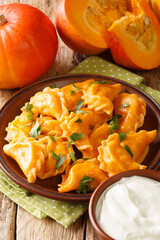 Autumn Pierogi pumpkin dumplings served with sour cream close-up in a plate on the table. vertical