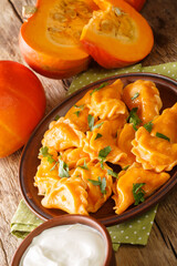 Homemade Ukrainian pumpkin dumplings served with sour cream close-up in a plate on the table. vertical