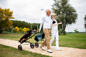 An elegant senior couple enjoying free time in retirement by playing golf and walking to the practice range. - Powered by Adobe