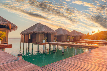 Sunset on Maldives island, luxury water villas resort hotel and wooden pier. Colorful sky and clouds and beach background for summer vacation holiday, traveling destination. Paradise sunset landscape