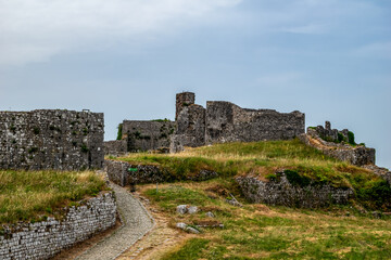 Fototapeta na wymiar Ruins of the medieval fortress of Shkoder on a cloudy summer day. The destroyed stone walls of the ancient Rozafa Castle among the green and yellow grass