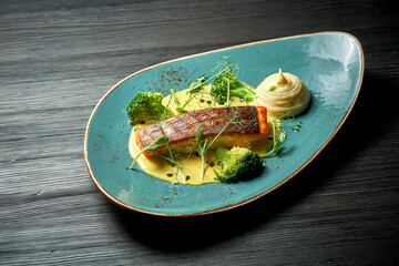 Salmon steak with yellow sauce, vegetable puree and broccoli. Wood background