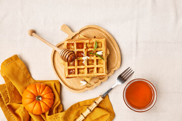Healthy autumn breakfast. Pumpkin spice Belgian waffles with orange honey on bamboo plate a shape of pumpkin on the table with linen tablecloth. Autumn season food flat lay. Top view.