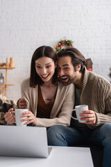 excited couple watching movie on laptop in living room with christmas decor
