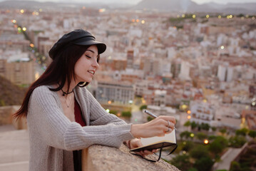 Woman writes in her note book phrases and thoughts outdoors at sunset