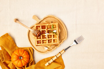 Healthy autumn breakfast. Pumpkin spice Belgian waffles with orange honey on bamboo plate a shape of pumpkin on the table with linen tablecloth. Autumn season food flat lay. Top view.