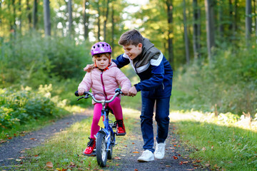 Cute little preschool girl in safety helmet riding bicycle. School kid boy, brother teaching happy...