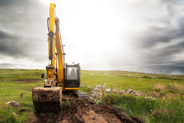 Medium size yellow excavator working in a green field. Building family house or farm in a country...