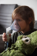 Przeziębiony chłopiec robiący inhalacje z misiem krokodylem © Katarzyna