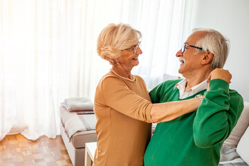 Obraz premium Carefree happy active old senior couple dancing jumping laughing in living room, cheerful retired elder husband holding hand of mature middle aged wife enjoy fun leisure retirement lifestyle at home