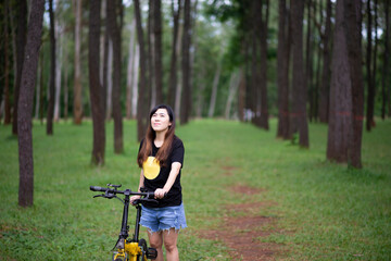 Fototapeta na wymiar Smiling Asia woman happy and relax time with bicycle outside the city, on the road in a pine forest on a summer day.