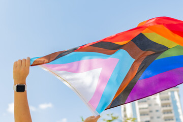 Progress pride flag (new design of rainbow flag) waving in the air with blue sky, Celebration of gay pride, The symbol of lesbian, gay, bisexual and transgender, LGBTQ community - obrazy, fototapety, plakaty