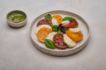 Caprese salad with red and yellow tomatoes, pesto, basil and mozzarella cheese in white plate, close up