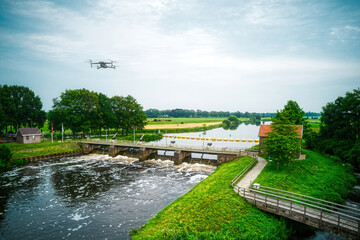 Water swirls from the weir in the river Vecht in the Netherlands. Downstream, Lock Keeper's House next to the bridge. Fish passage, Overijsselse Vecht, A flying drone in the blue sky