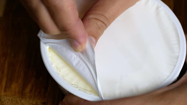 The woman opens a plastic jar with white cheese, cottage cheese, yogurt. Healthy dairy food.