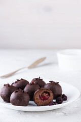 Truffles with cherries in chocolate on a white plate.