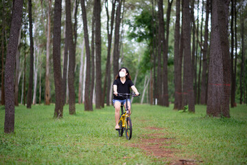 Asia woman riding a bicycle and wearing a face mask against covid-19 outside the city, on the road in a pine forest on a summer day. Lifestyle Concept