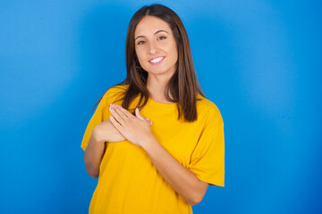 Honest Young european brunette woman wearing yellow T-shirt on blue background keeps hands on...