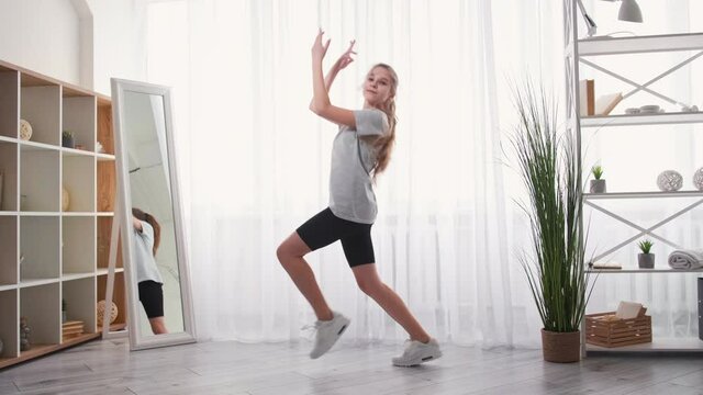 Hip-hop dance. Home fitness. Enjoy training. Happy teenager girl moving on music feeling joy in light room interior.