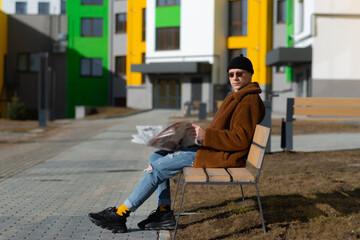 Young man reading newspaper on park bench