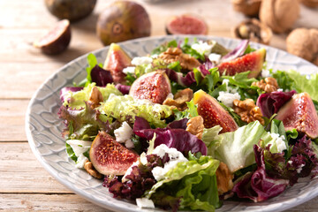 Figs salad with cheese and walnuts on wooden table.