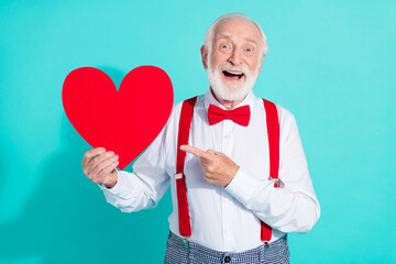 Portrait of attractive trendy cheerful mister holding in hand demonstrating heart isolated over bright teal turquoise color background