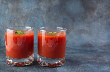 Two glasses with tomato juice on a blue grunge background. Copy space.